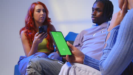 Close-Up-Of-Woman-With-Green-Screen-Mobile-Phone-Sitting-With-Gen-Z-Friends-Talking-And-Sharing-Posts